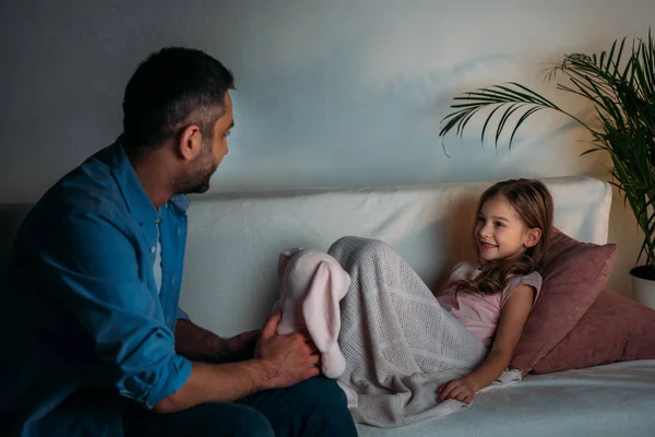 Vue latérale de fille souriante regardant père avec jouet dans les mains à la maison — Photo de stock