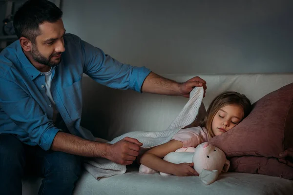 Padre cubriendo durmiendo hija con manta - foto de stock