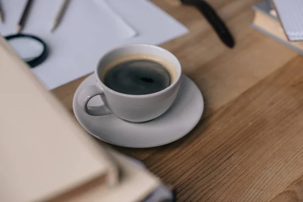 Primer plano de la taza de café en el escritorio con pila de libros - foto de stock