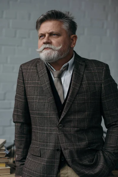 Seniorchef im stylischen Tweed-Anzug blickt vor weißer Backsteinwand weg — Stockfoto