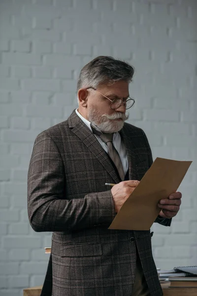 Uomo anziano in tweed vestito lettera di scrittura davanti al muro di mattoni bianchi — Foto stock