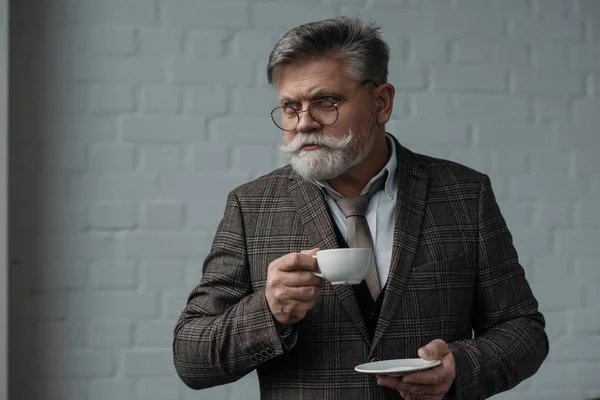 Bell'uomo anziano con tazza di caffè davanti al muro di mattoni bianchi — Foto stock