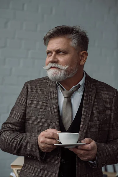 Senior avec une tasse de café devant un mur de briques blanches — Photo de stock