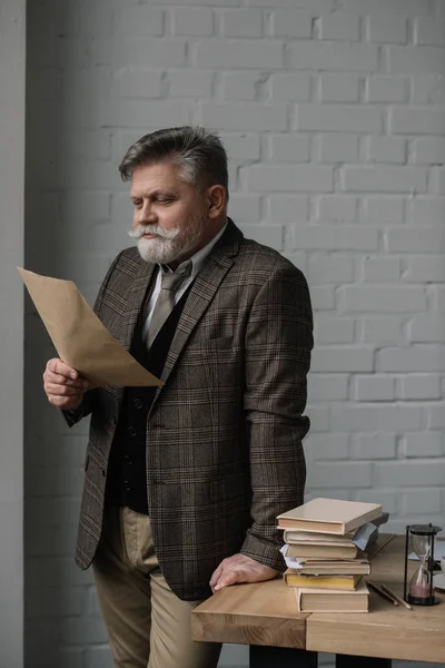 Hombre mayor leyendo carta mientras se inclina en el escritorio - foto de stock