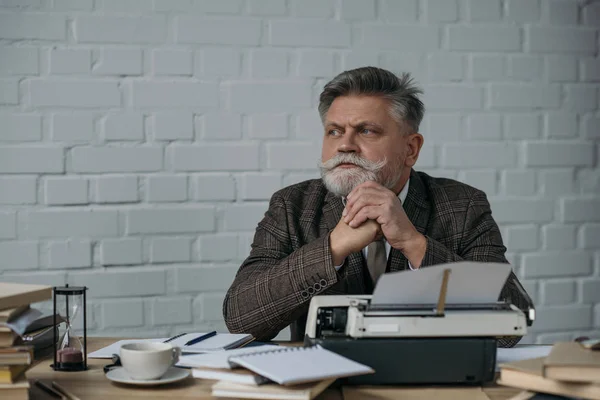 Écrivain chevronné réfléchi assis sur le lieu de travail et regardant loin — Photo de stock