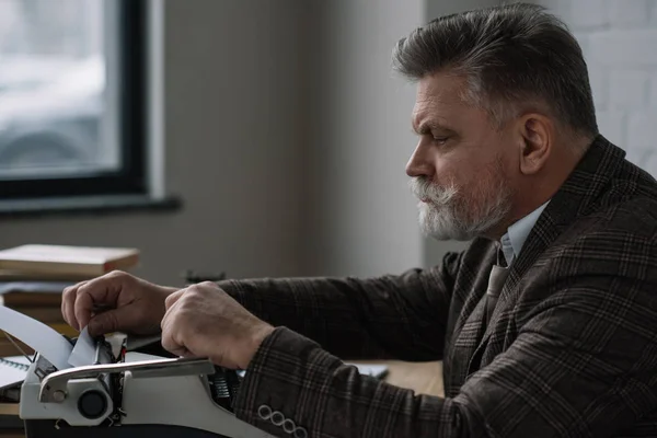 Handsome senior writer loading paper into typewriter — Stock Photo