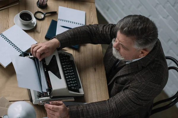 High angle view of senior writer loading paper into typewriter — Stock Photo