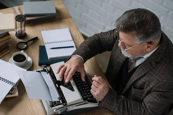 Vista de ángulo alto del escritor senior que trabaja con máquina de escribir - foto de stock