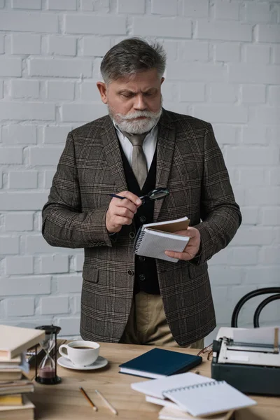 Focused senior writer reading manuscript with magnifying glass — Stock Photo