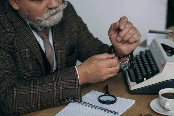 Schnappschuss eines älteren Schriftstellers, der am Arbeitsplatz seine Oldtimer-Uhr aufsetzt — Stockfoto