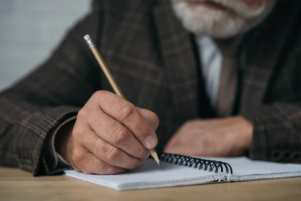 Close-up shot of senior man writing in notebook with pencil — Stock Photo