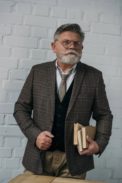 Elegante uomo anziano in abito tweed con pila di libri — Foto stock