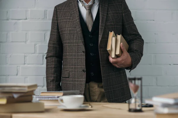 Cropped shot of man in tweed costume holding stack of books — Stock Photo