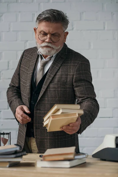 Thoughtful senior writer holding stack of books — Stock Photo