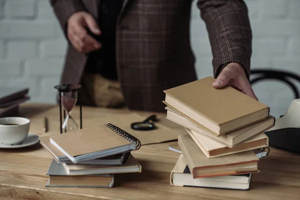 Обрезанный снимок человека, берущего стопку книг со стола — стоковое фото