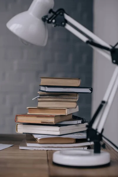 Primer plano de los libros apilados y la lámpara de mesa en el escritorio - foto de stock