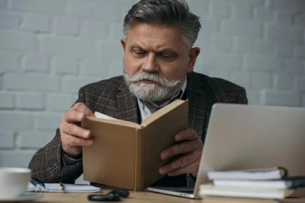 Grave sênior escritor leitura livro no local de trabalho — Fotografia de Stock