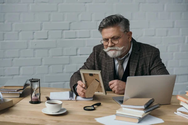 Старший писатель смотрит на фотографию в рамке на своем рабочем месте — стоковое фото