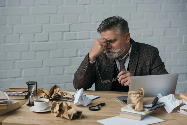 Scrittore anziano oberato di lavoro seduto sul posto di lavoro disordinato — Foto stock