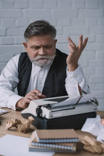 Scrittore anziano depresso che prova a lavorare con la macchina da scrivere sul posto di lavoro disordinato — Foto stock