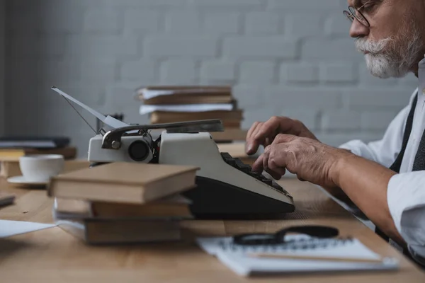 Vista lateral del escritor senior serio que trabaja con la máquina de escribir - foto de stock