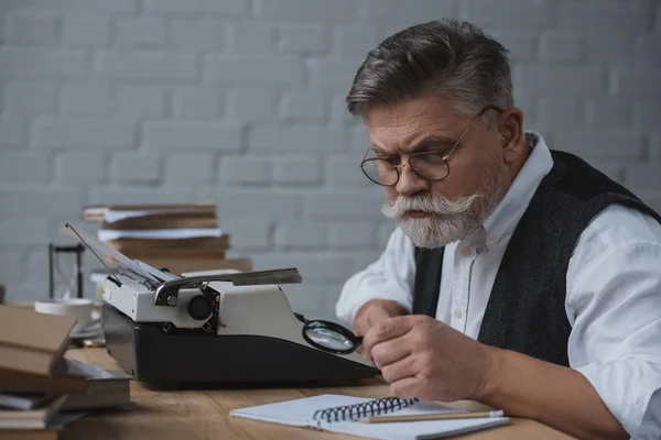 Старший писатель переписывает рукопись с помощью печатной машины — стоковое фото