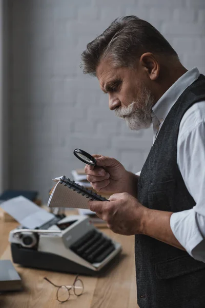 Senior writer reading manuscript with magnifying glass — Stock Photo