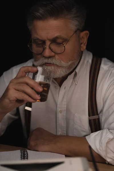 Guapo hombre mayor bebiendo whisky en negro - foto de stock