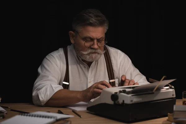 Écrivain senior travaillant avec machine à écrire isolé sur noir — Photo de stock