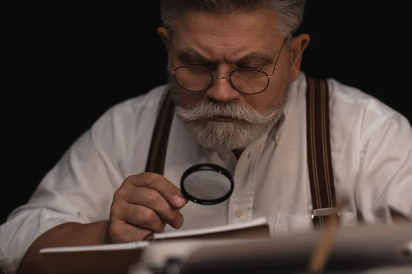 Close-up portrait of senior writer reading manuscript in notebook with magnifying glass — Stock Photo