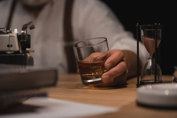 Colpo ritagliato di scrittore senior con un bicchiere di whisky in mano sul posto di lavoro — Foto stock