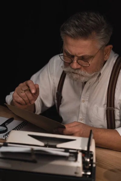 Grave écrivain principal travaillant avec manuscrit isolé sur noir — Photo de stock