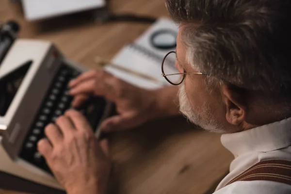 Primer plano del escritor senior que trabaja con la máquina de escribir - foto de stock