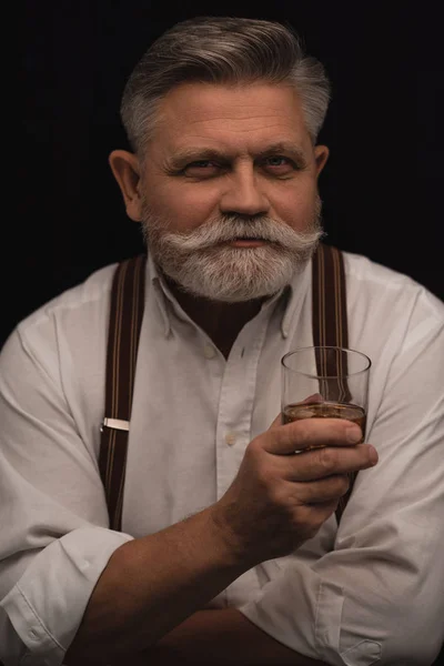 Elegante uomo anziano con bicchiere di whisky isolato su nero — Foto stock