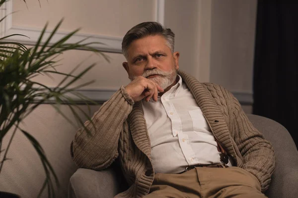 Handsome senior man sitting in armchair and looking at camera — Stock Photo