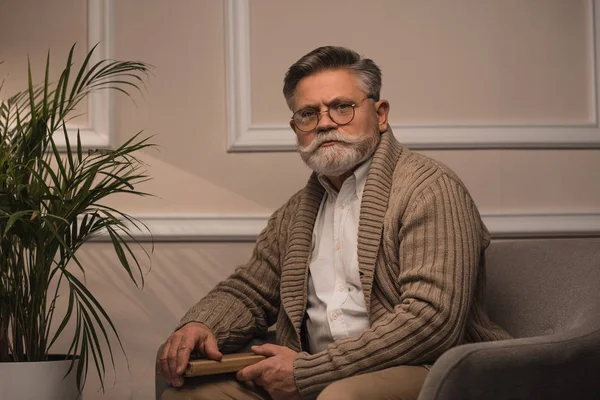 Senior man sitting in cozy armchair and looking at camera — Stock Photo