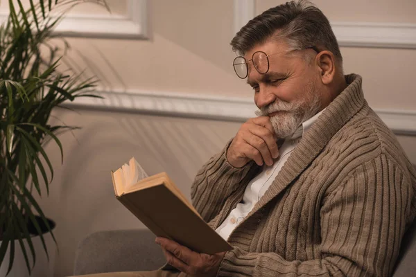 Hombre mayor feliz en suéter libro de lectura - foto de stock