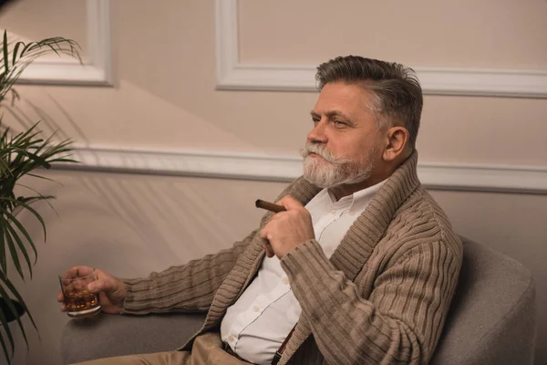 Senior man smoking cigar and drinking whiskey in armchair — Stock Photo