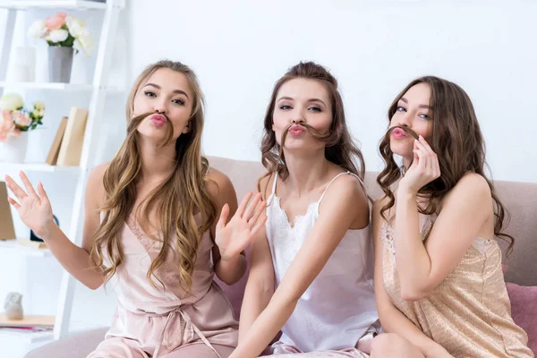 Beautiful young women in pajamas holding hair as moustaches and smiling at camera — Stock Photo