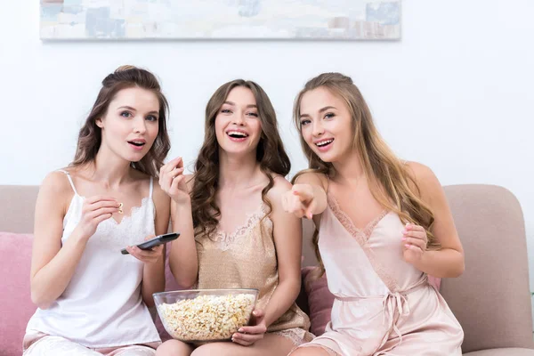 Belles petites amies heureuses en pyjama manger du pop-corn et rire tout en regardant la télévision — Stock Photo