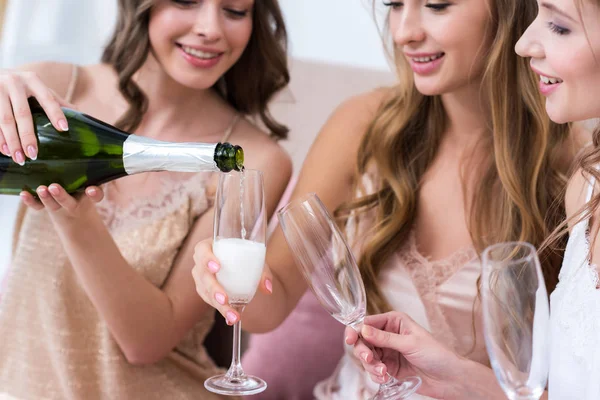 Recortado disparo de hermosa sonriente novias en pijama verter champán en vasos - foto de stock
