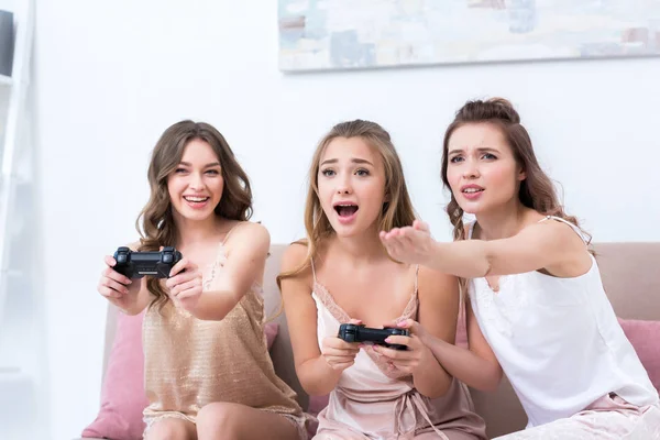 Jeunes femmes émotionnelles en pyjama jouant avec des joysticks ensemble à la maison — Stock Photo