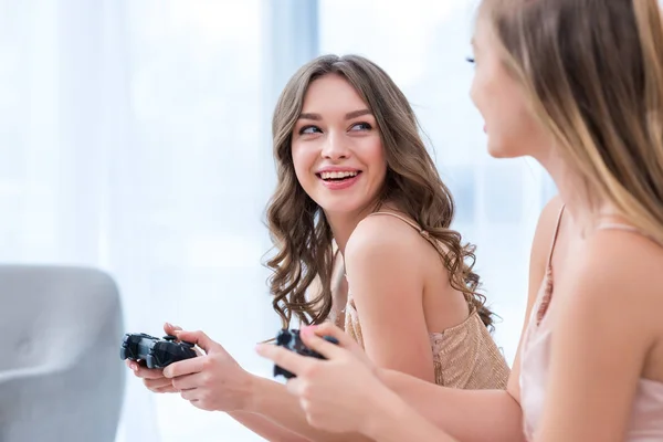 Chicas sonrientes atractivas jugando con joysticks en pijama party - foto de stock