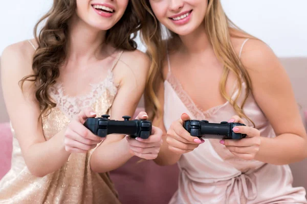 Tiro recortado de mulheres jovens sorridentes brincando com joysticks na festa do pijama — Fotografia de Stock