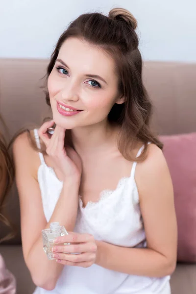 Hermosa mujer joven sosteniendo botella de perfume y sonriendo a la cámara — Stock Photo