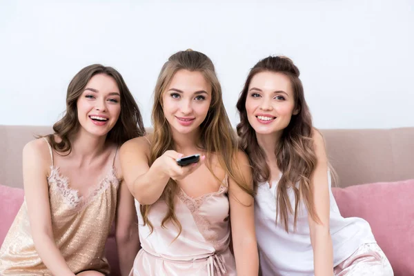 Schöne junge Frauen im Schlafanzug mit Fernbedienung und lächelnd in die Kamera — Stockfoto
