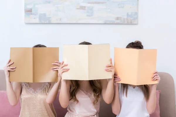 Three young women in pajamas hiding faces behind magazines with blank covers — Stock Photo