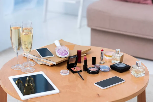 Vista de cerca de los dispositivos digitales, copas de champán y cosméticos en la mesa - foto de stock