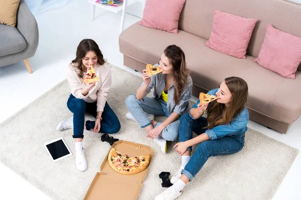 Vista de ángulo alto de hermosas mujeres jóvenes sonrientes comiendo pizza en casa - foto de stock