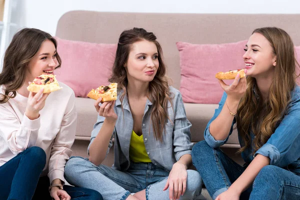 Schöne lächelnde Freundinnen, die Pizza essen und einander anschauen — Stockfoto